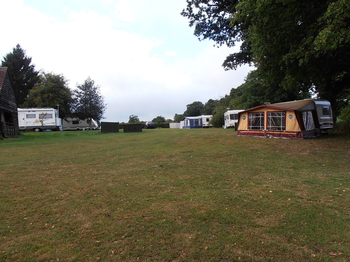 The Certificated Location field at Goffsland Farm with touring caravans and a motorhome pitched under mature oak trees, a timber barn on the left