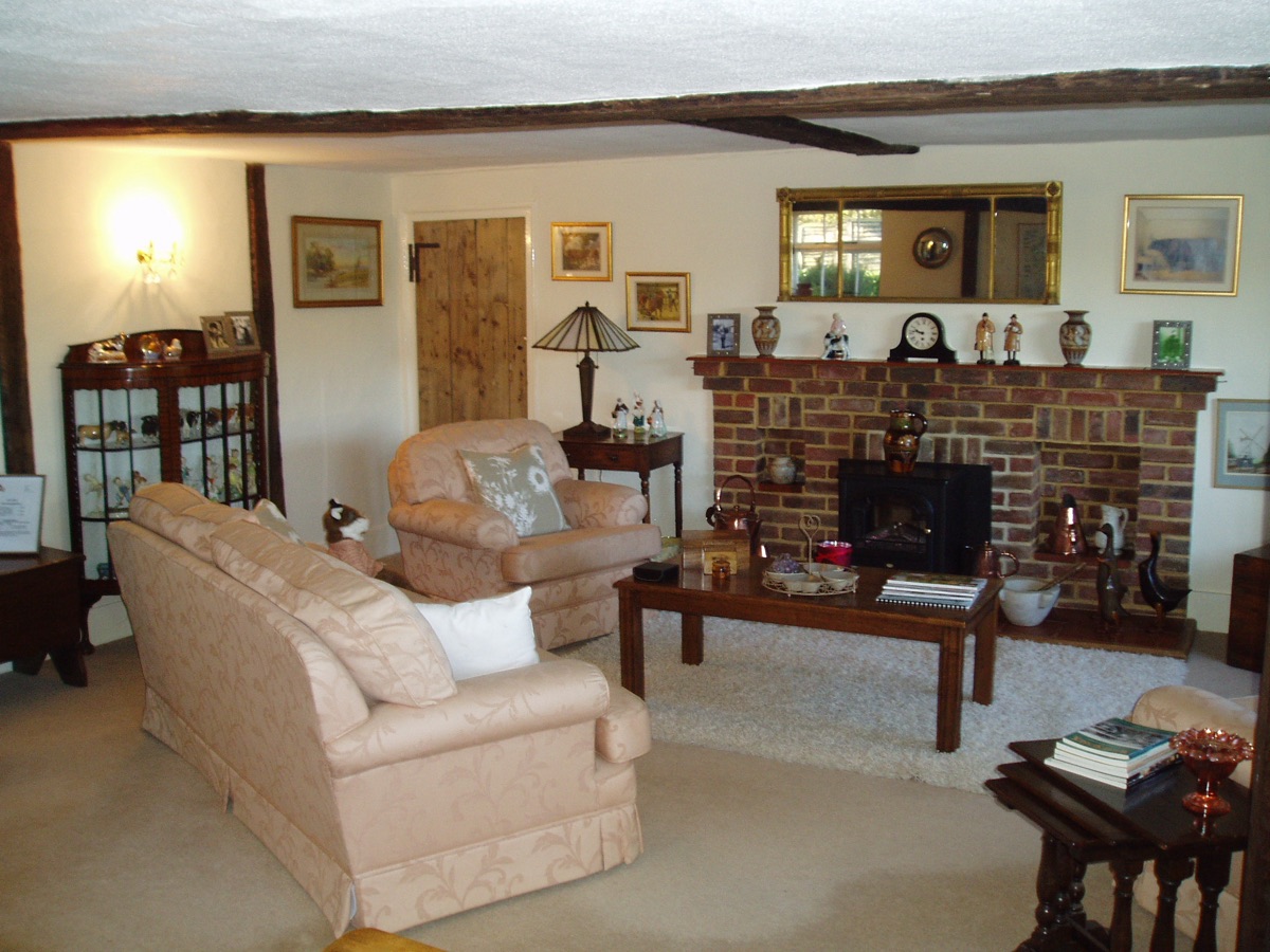 Inside the Grade II listed farmhouse at Goffsland Farm: a heavy oak beam spans the ceiling above a wide brick fireplace with a stove set into it